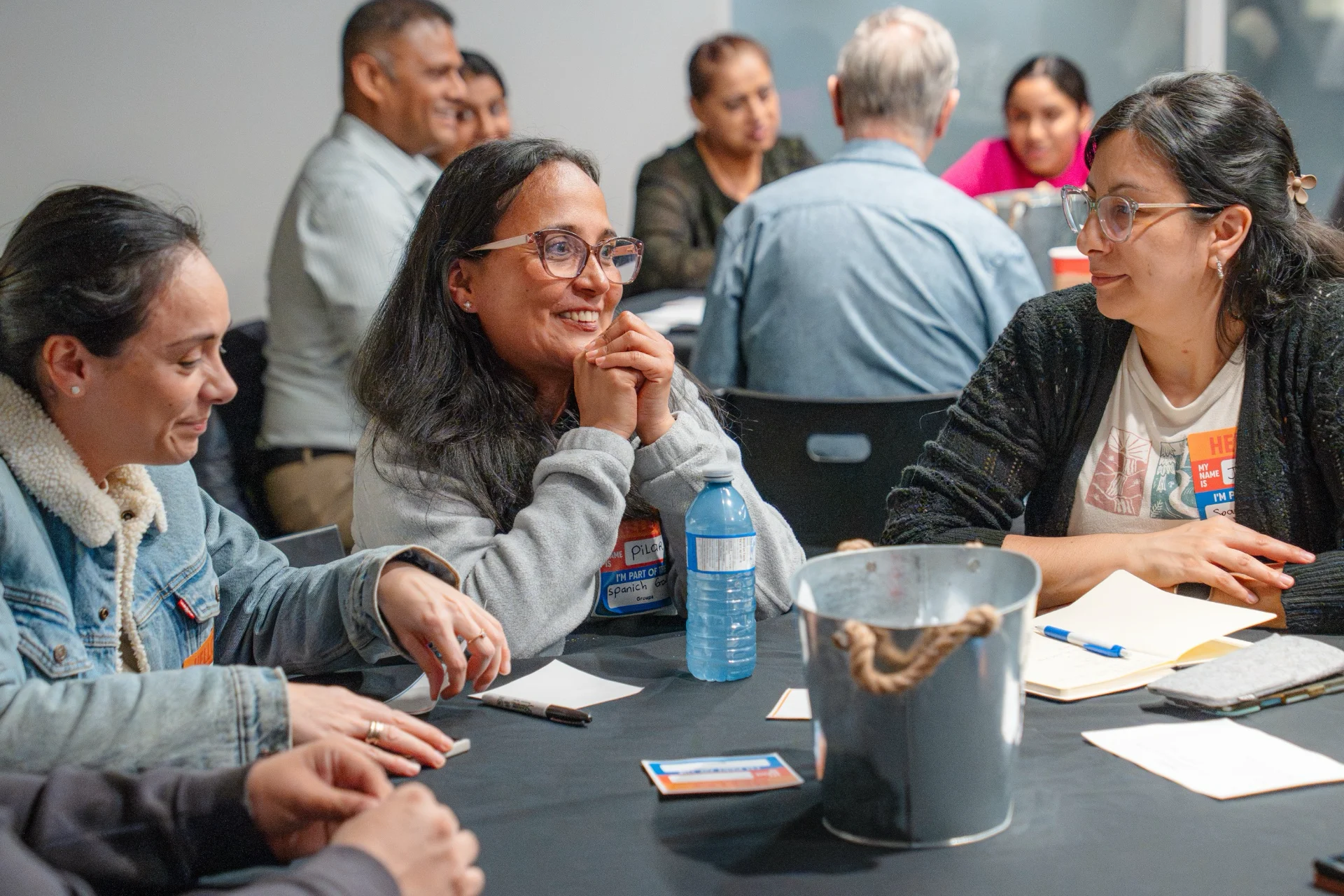 Three women wearing name tags smiling and talking together at a table during a group gathering.