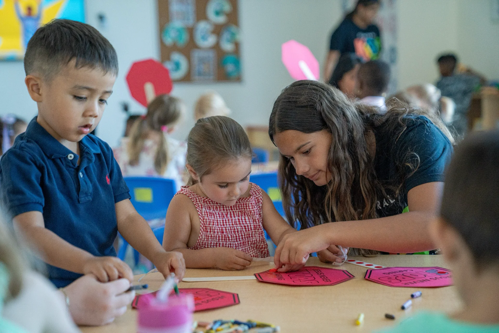 A volunteer helping two young children with a craft activity in a kids ministry room.