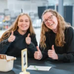 Two young adults at a numbered table giving thumbs up and smiling.